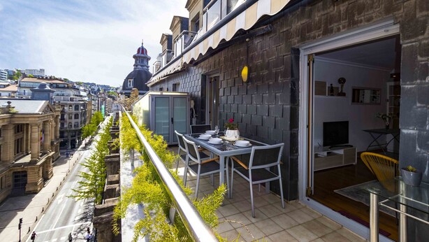 A rooftop terrace with a dining table and chairs, a yellow chair, and a view of the cityscape. - Aire de La Concha | The Rentals Collection (San Sebastián)