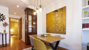 A dining area with a wooden table, yellow chairs, and a large abstract painting on the wall. - Aire de La Concha | The Rentals Collection (San Sebastián)