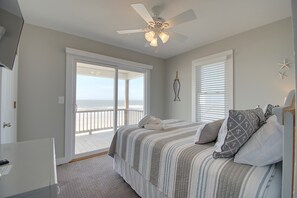 Een slaapkamer met een bed, een plafondventilator, een raam met zonwering en uitzicht op het strand.