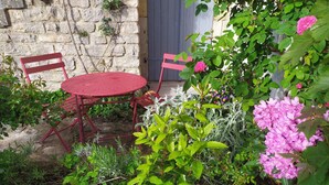 Un giardino con un tavolo e sedie in metallo rosso, circondato da diverse piante e fiori.