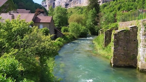 Un fiume che scorre attraverso una cittadina con edifici in pietra e una scogliera sullo sfondo.