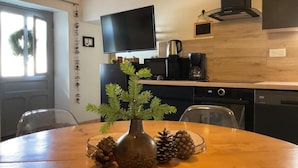 Una cucina moderna con un tavolo in legno, un vaso con pigne e un televisore appeso al muro.