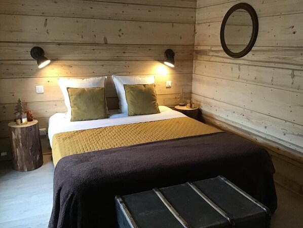 A wooden cabin-style bedroom with a bed, two bedside lamps, a round mirror, and a bench. - Au Charmant Chablis (Champagnole)