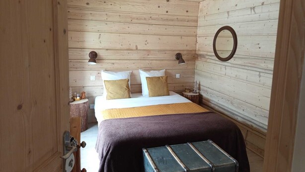 Camera da letto con rivestimento in legno, un letto, due lampade da comodino, uno specchio rotondo e un piccolo tavolo con lampada.