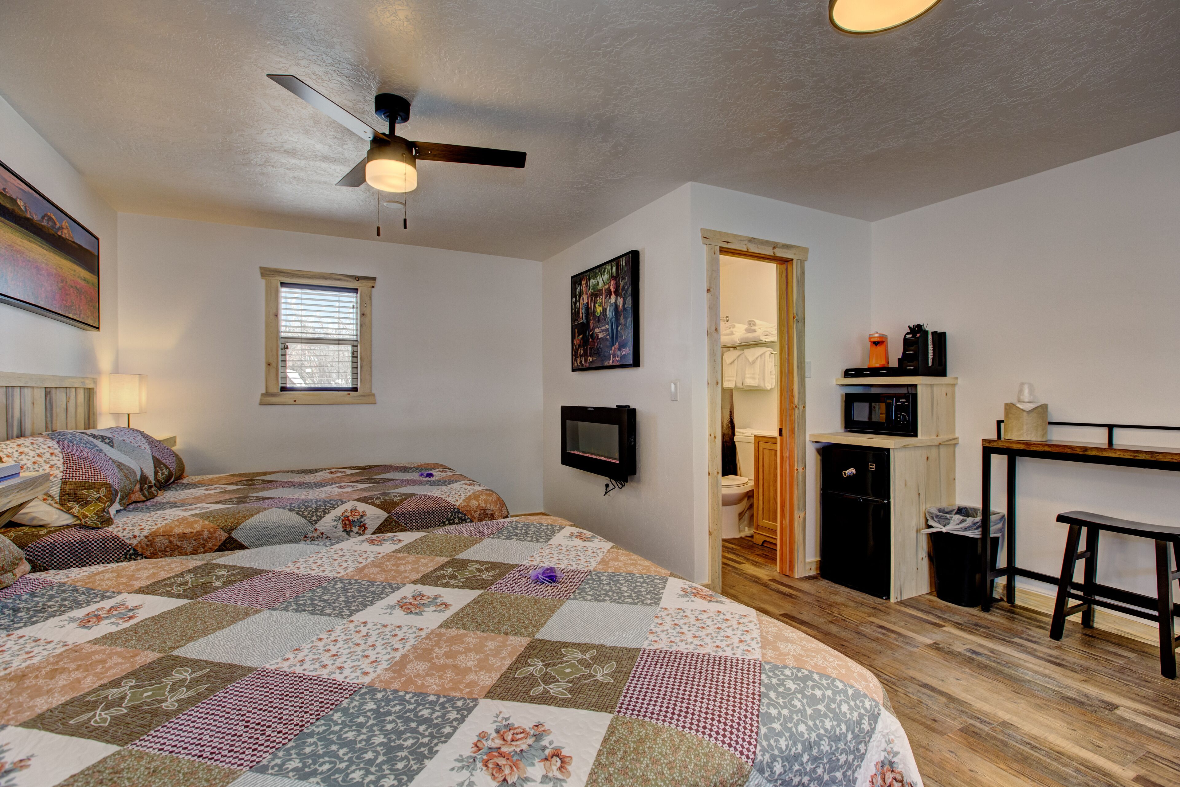 Un dormitorio con una cama grande, ventilador de techo, televisión, ventana y kitchenette.