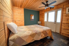 A wooden room with a bed, a ceiling fan, a door, and a mirror.