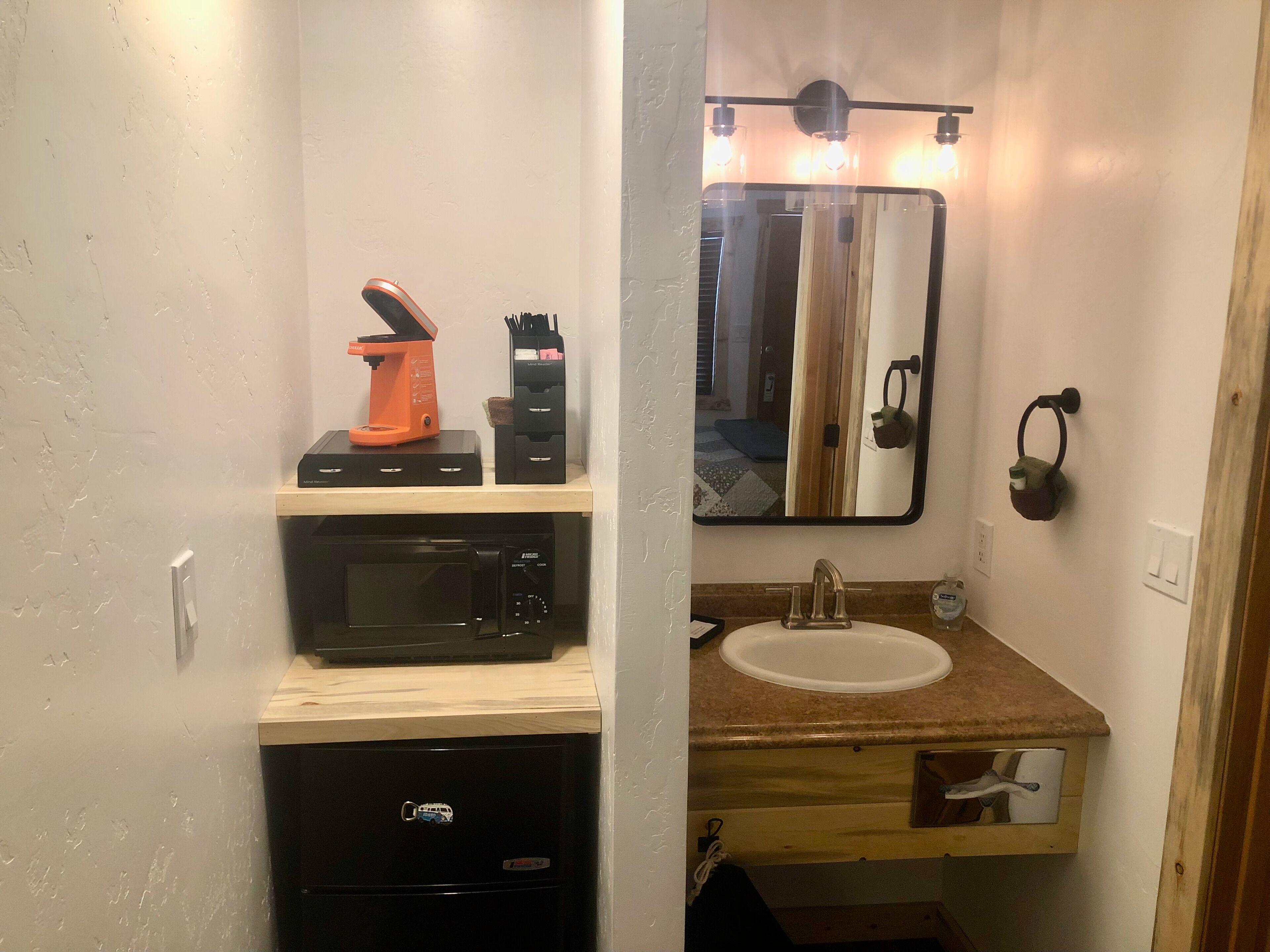 Een kleine badkamer met een wastafel, spiegel en een koffiezetapparaat op een plank.