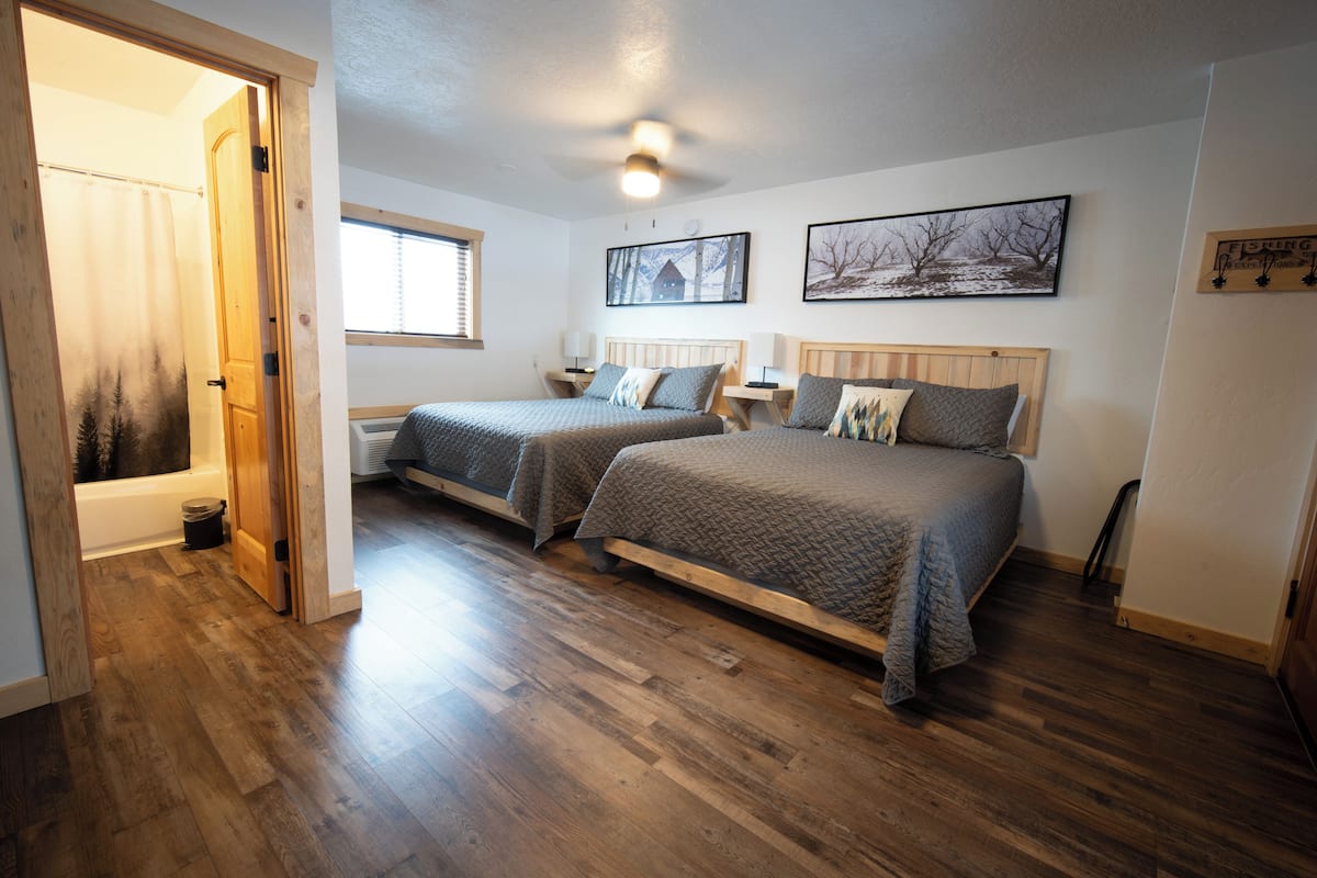 A bedroom with two beds, wooden flooring, a ceiling fan, and a window with blinds.