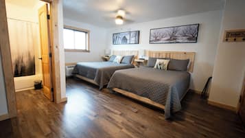A bedroom with two beds, wooden flooring, a ceiling fan, and a window with blinds.