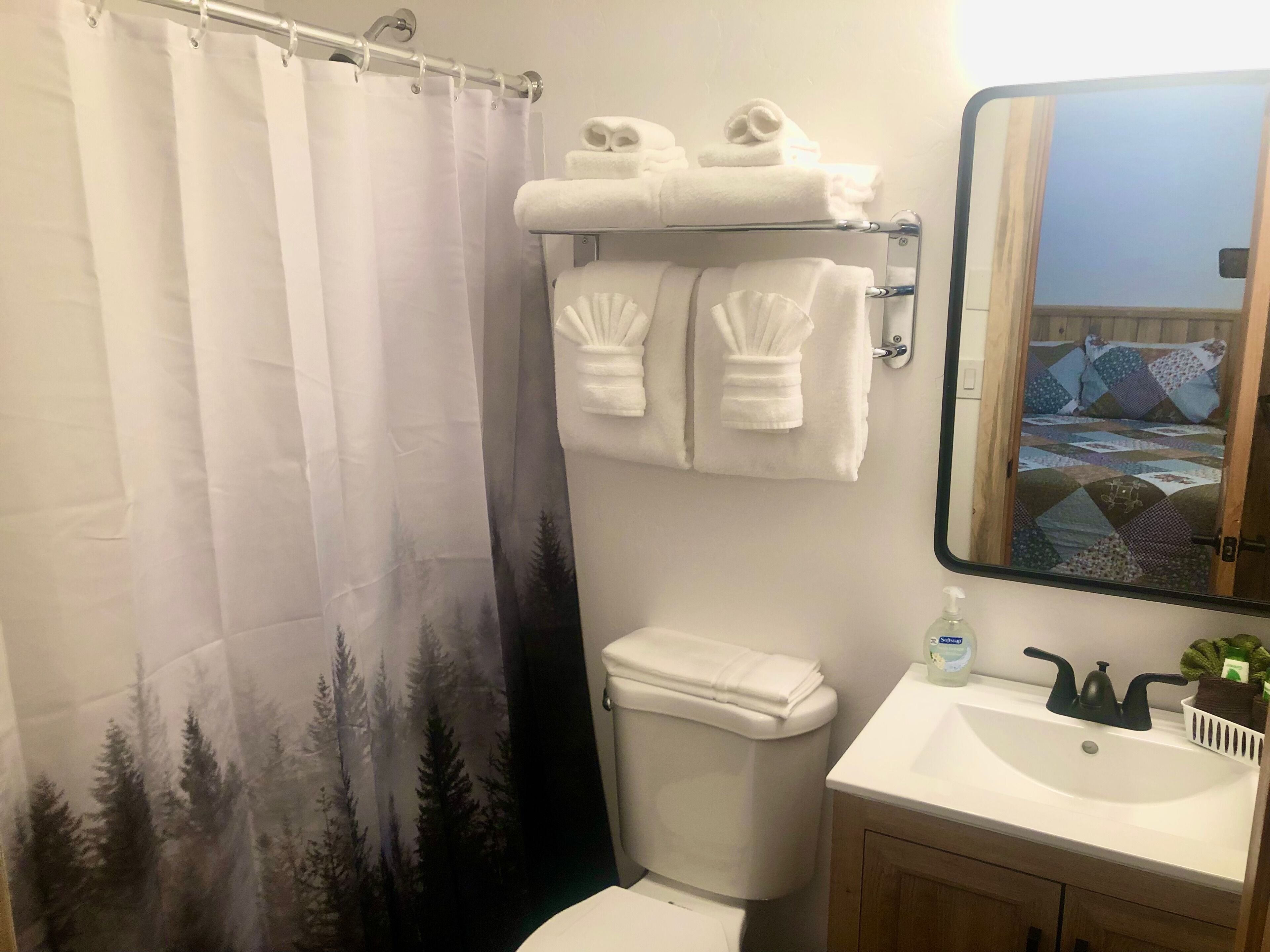 A bathroom with a shower curtain, a toilet, a sink with a soap dispenser, and a towel rack with towels.