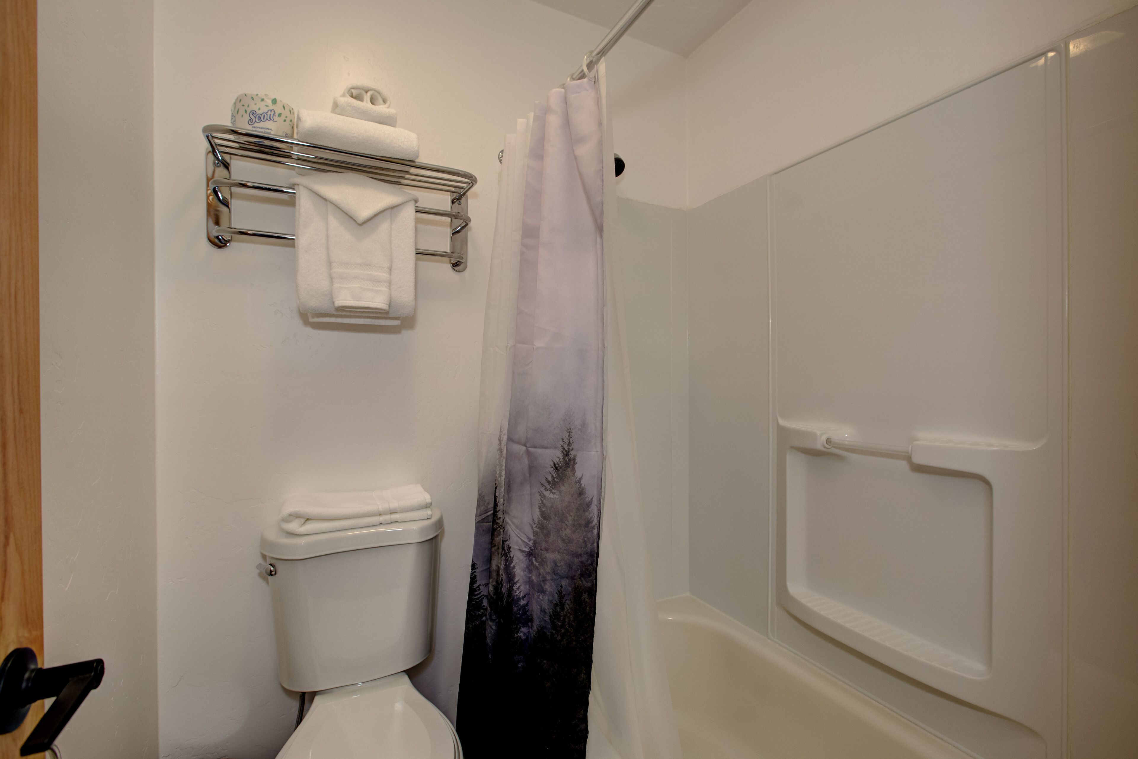 Un baño con inodoro, cortina de ducha con diseño de bosque y toallero con toallas.