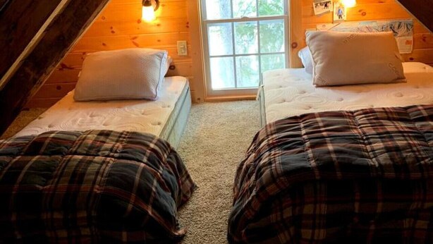 Une chambre mansardée chaleureuse avec deux lits, une fenêtre et des murs en bois.
