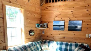 L’intérieur chaleureux d’un chalet avec un grand canapé à carreaux, une table basse en bois et deux photographies encadrées accrochées au mur.