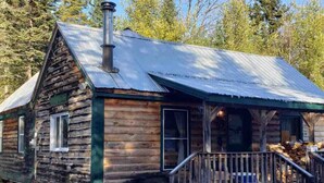 Une cabane rustique en rondins de bois, dotée d’une cheminée, d’un porche et d’un sol recouvert de neige.