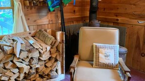 L’intérieur chaleureux d’un chalet avec un fauteuil, une pile de bois de chauffage, une pagaie et une cheminée.