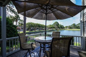 Relax on the deck with a round table and two chairs, shaded by a large umbrella, overlooking a serene body of water.