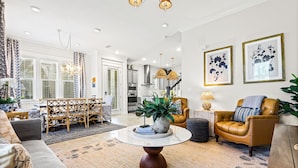 A modern living room with a round coffee table, a sofa, a leather armchair, and a dining area with a wooden table and chairs.