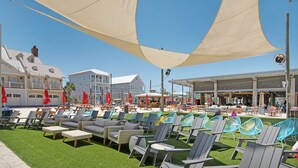 A beachside resort with outdoor seating areas, including lounge chairs and tables, shaded by large canopies.