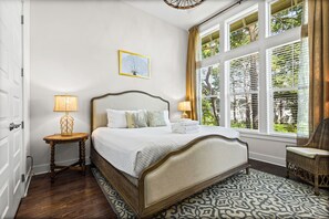 Un dormitorio con cama, dos mesitas de noche, una ventana con persianas, una silla y un tapete estampado.