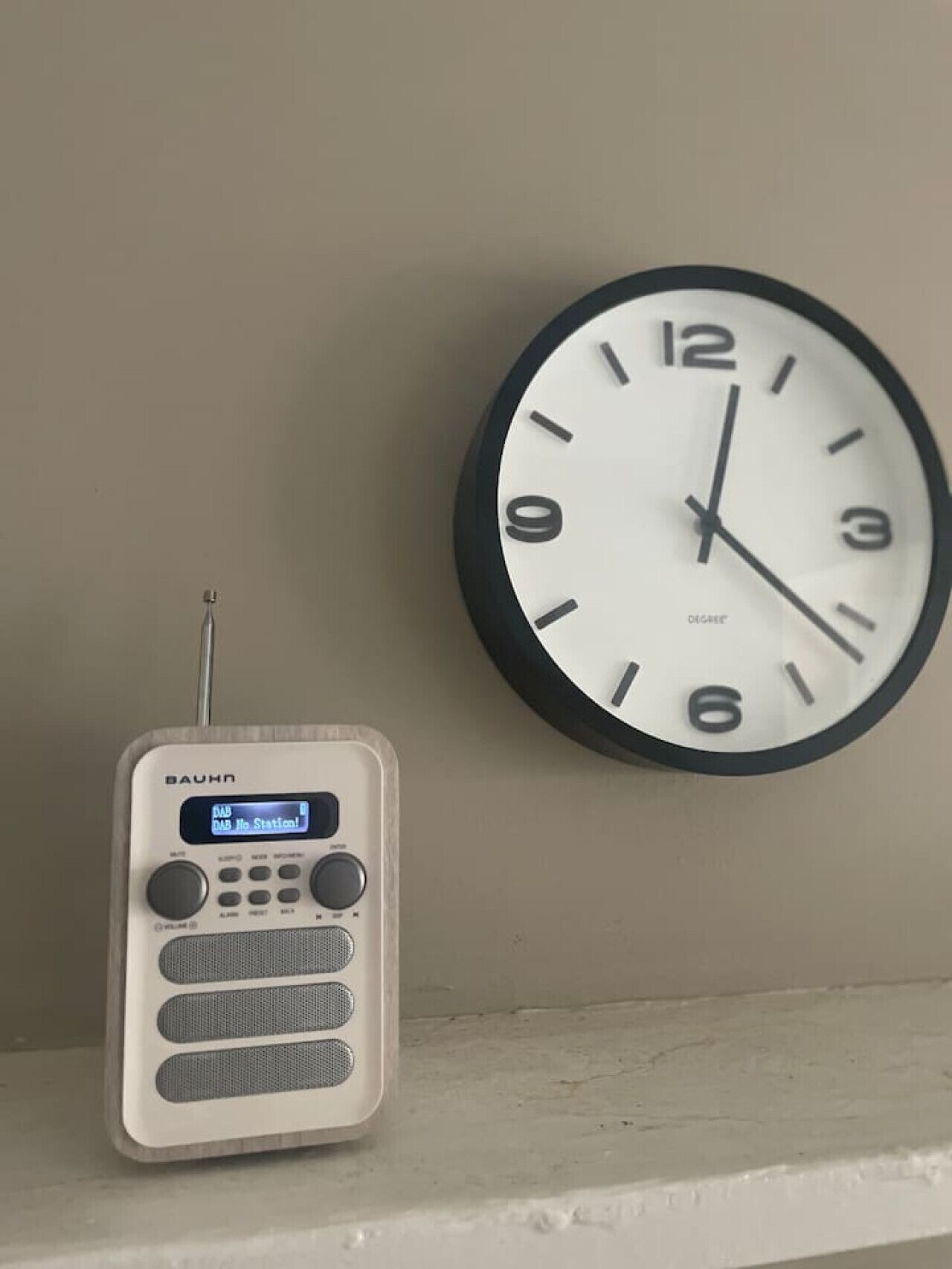 Un reloj de pared y una radio sobre una estantería.