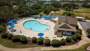 A swimming pool with lounge chairs and umbrellas, surrounded by well-maintained bushes and a building with a pitched roof. - Gone Coastal: Dog-Friendly (2 max), Private Pool (Corolla)