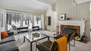 Een moderne woonkamer met een open haard, grote ramen en een gezellige zithoek.