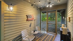 Een overdekt terras met metalen stoelen en een tafel, een wandlamp en een decoratief wandobject.