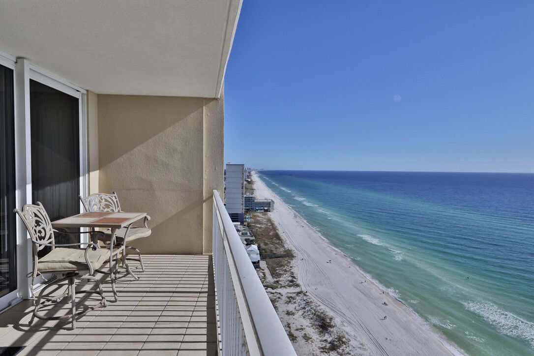 A balcony with a table and chairs overlooking a beach.