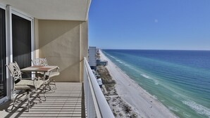 A balcony with a table and chairs overlooking a beach. - 3BR 3.5BA @ EMERALD BEACH! SLEEPS 10! (Panama City Beach)