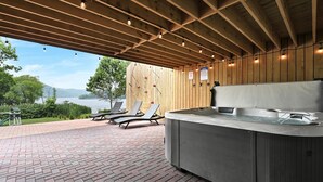 An outdoor hot tub area with a wooden deck, lounge chairs, and a view of a lake.