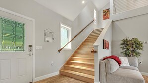 A modern interior with a wooden staircase, a grey sofa with a red throw, and a large window with green foliage view.