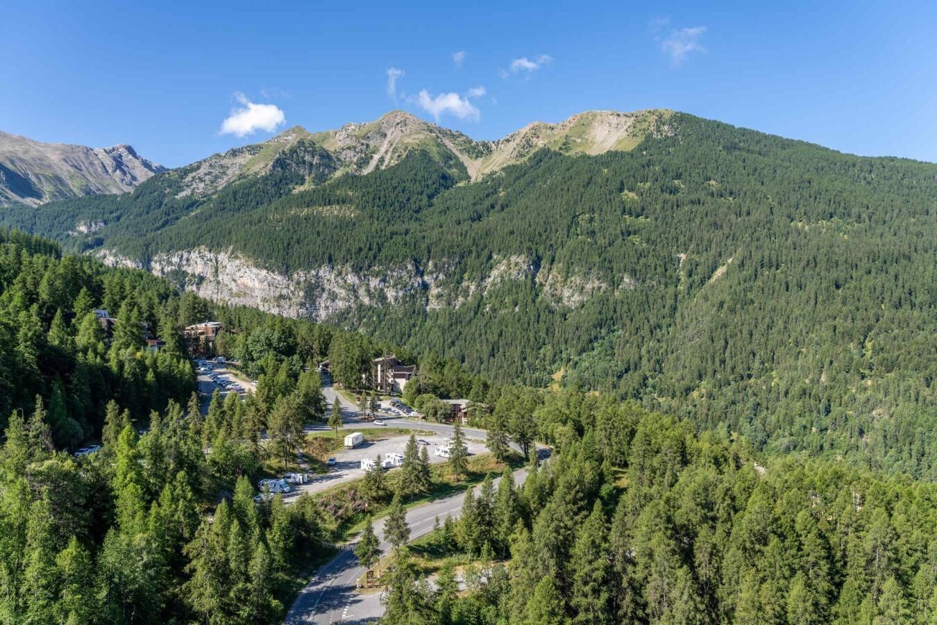 A mountain lodge with a road leading to it, surrounded by dense forest and mountains.
