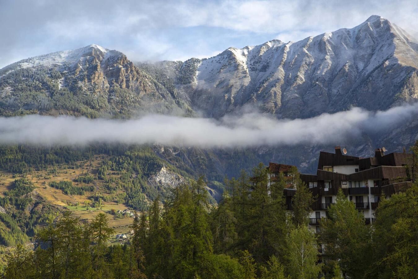 A mountain landscape with a valley, a building with multiple floors, and a forested area in the foreground.