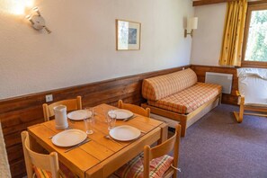 Una habitación acogedora con una mesa de comedor de madera dispuesta para cuatro personas, un banco con cojín a cuadros y una ventana con cortinas.