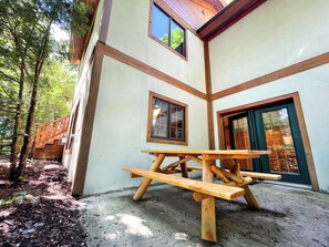 A wooden picnic table in front of a building with a green door and windows.
