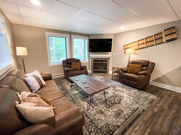 A living room with a brown leather sofa, two armchairs, a coffee table, a fireplace, and a flat-screen TV.