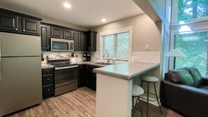 A modern kitchen with dark cabinets, stainless steel appliances, a wooden floor, and a bar area with stools. - Ski in on Boyneland Run, Slps 18, Fully remodeled (Boyne Falls)