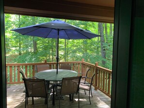 A wooden deck with a round table and four chairs, an umbrella, and a view of a forested area.