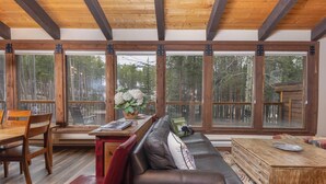 Ein Zimmer mit Holzbalkendecke, großen Fenstern, einer Couch, einem Esstisch und einer Bank.