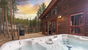Eine Holzhütte mit Whirlpool, Terrasse und Wald im Hintergrund.