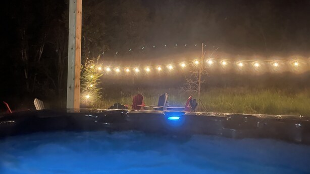 A hot tub with a blue light, surrounded by string lights and a wooden pole.