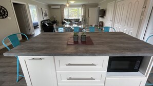 A modern kitchen with a central island, white cabinetry, a microwave, and blue chairs.
