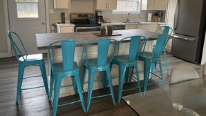 A modern kitchen with a central island, teal chairs, and a stainless steel refrigerator.