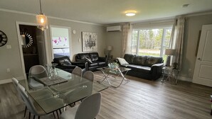 A spacious living area with a glass dining table, leather sofas, and a large window providing natural light.