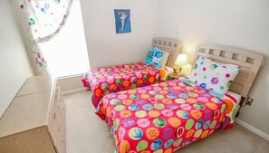 A bedroom with two beds, each with colorful polka dot bedding, a nightstand with a lamp, and a small wall decoration.