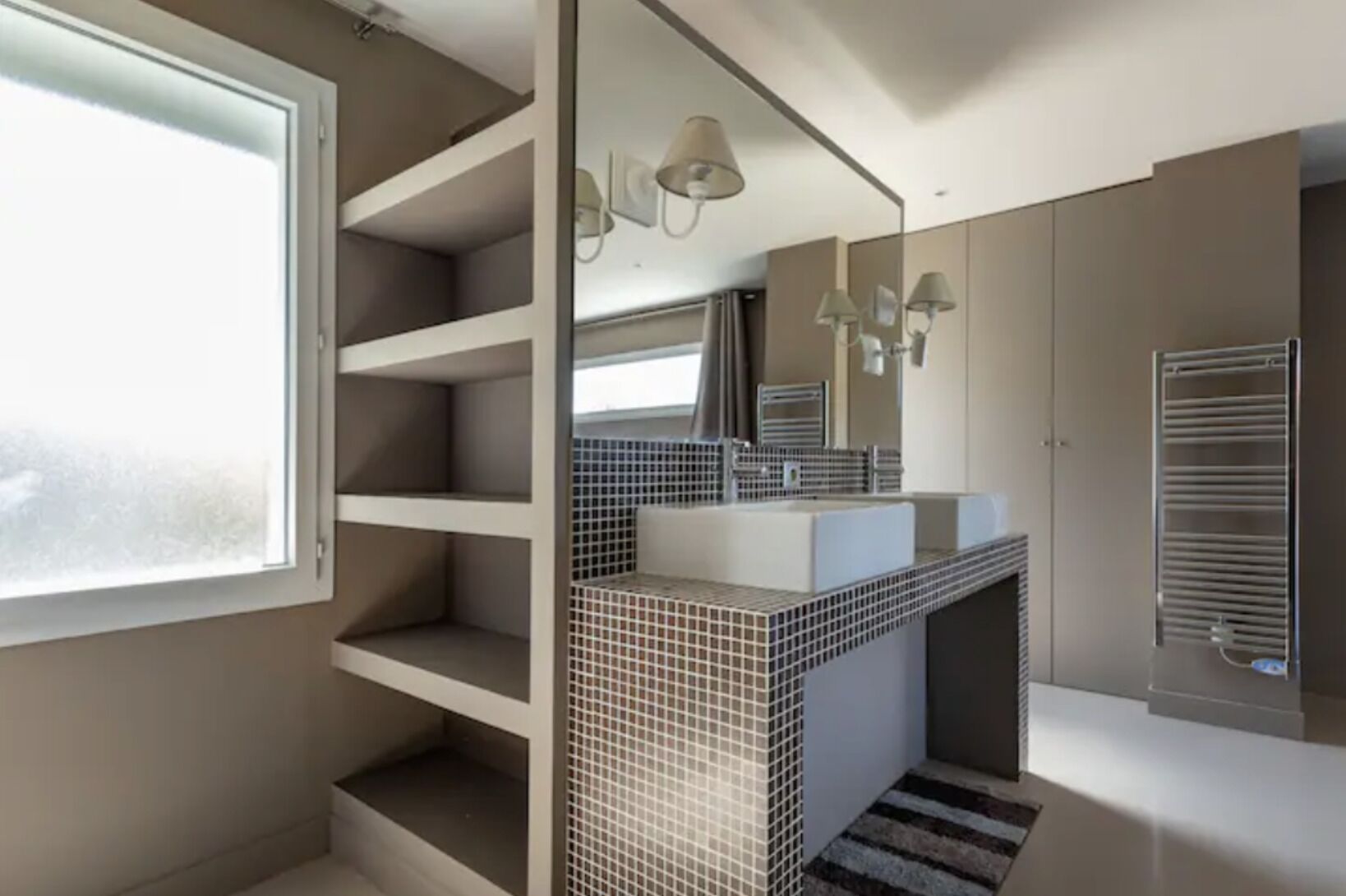 A modern bathroom with a large window, a tiled backsplash, a sink with a mirror, and a towel rack.