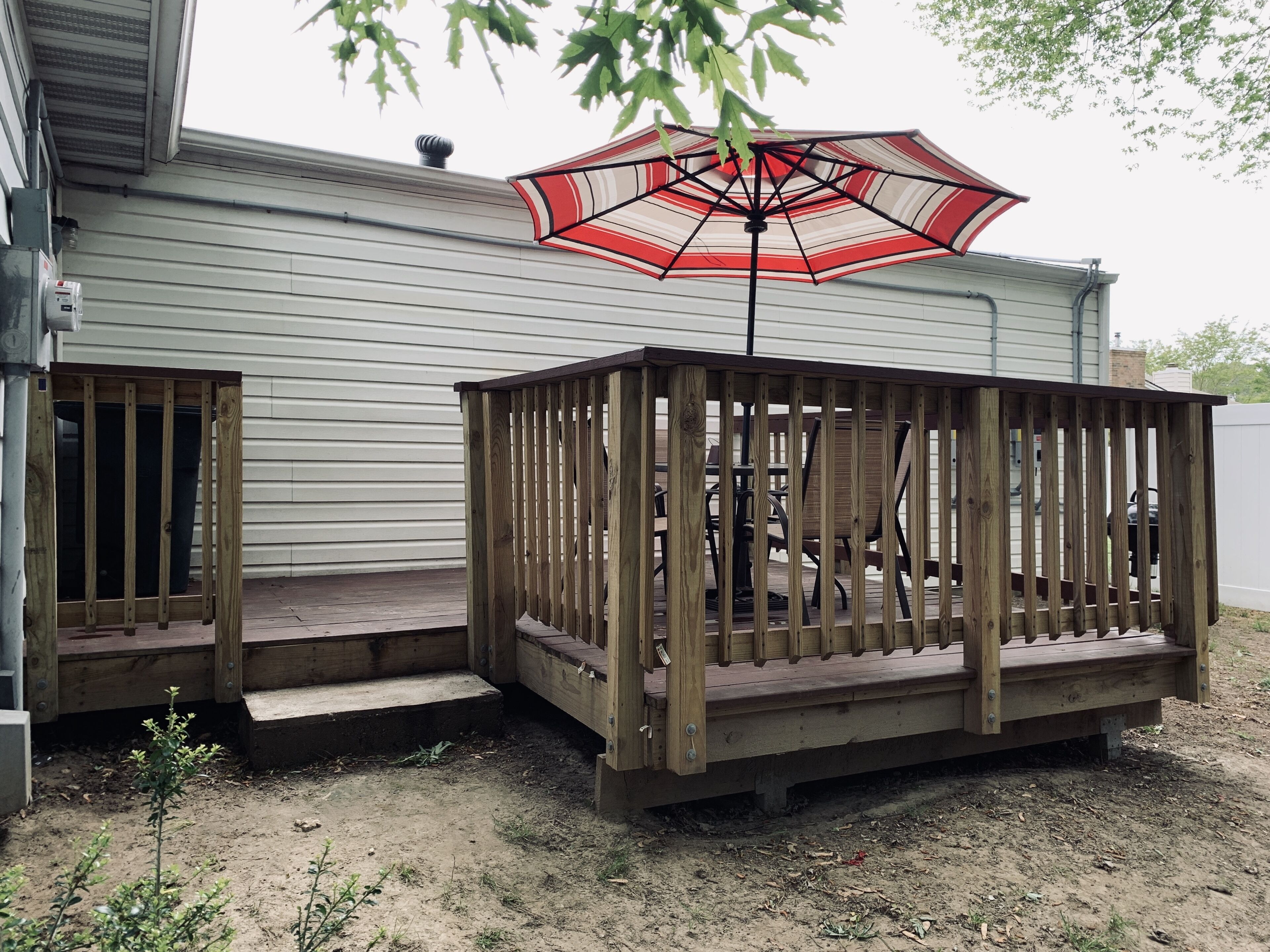 A wooden deck with a table and chairs, a covered patio area, and a view of a house in the background.