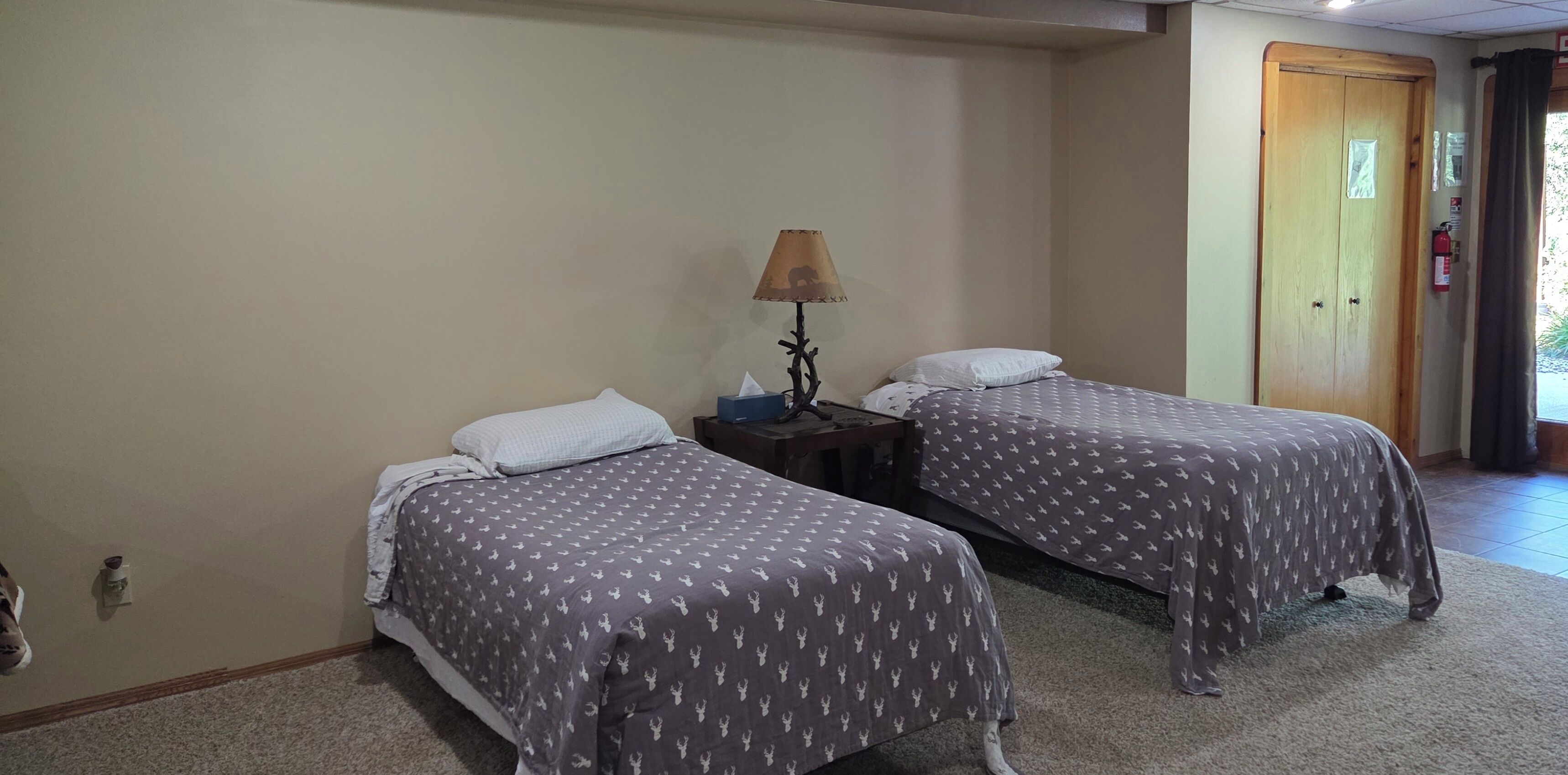 A room with two beds, each with a patterned bedspread, a bedside table with a lamp, and a door to the right.