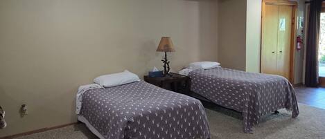 A room with two beds, each with a patterned bedspread, a bedside table with a lamp, and a door to the right.