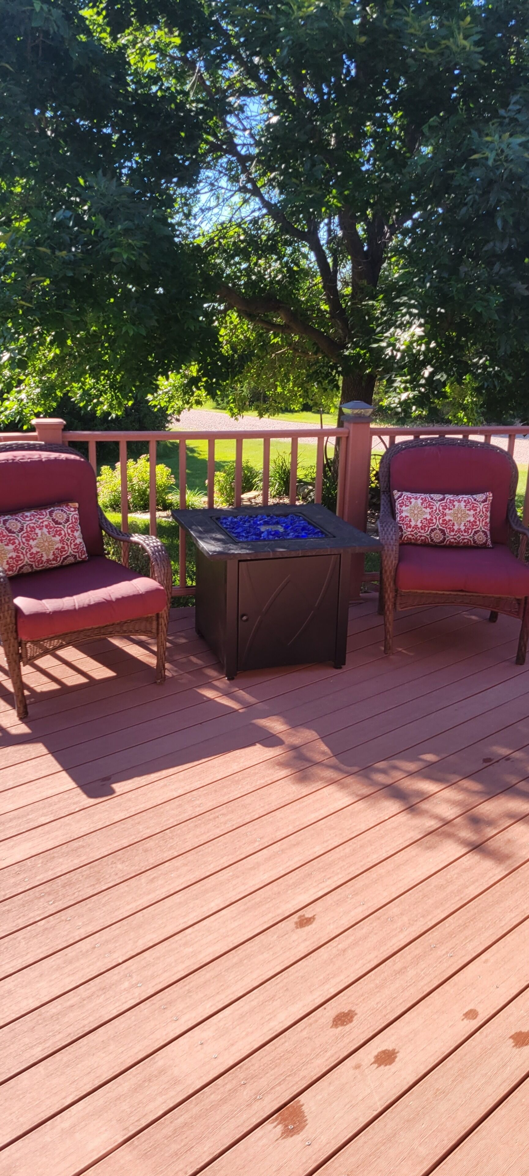 Eine Holzterrasse mit zwei Korbstühlen und einem Tisch mit blauer Glasplatte.